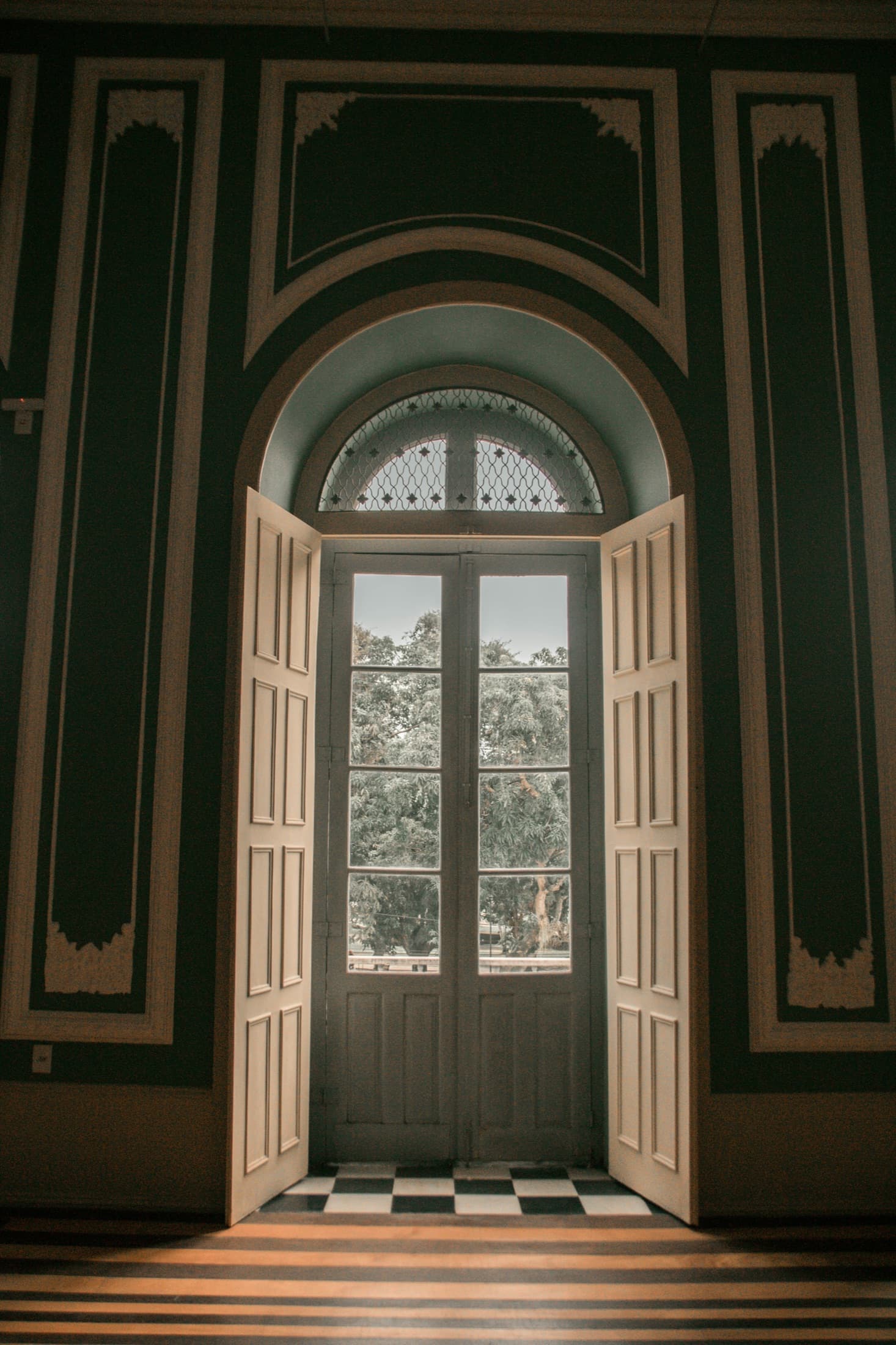 Puerta doble acristalada bajo un arco, con paredes verde oscuro y suelo de damero