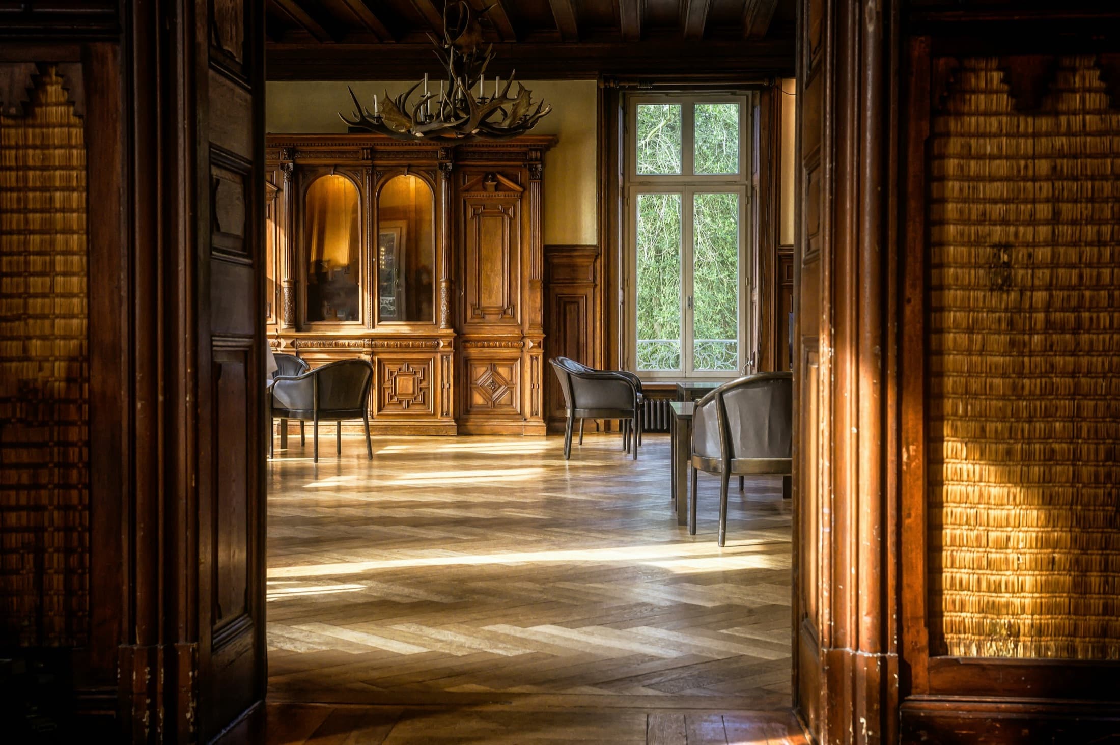 Salón clásico con paneles de madera, lámpara de araña y suelo de parquet visto desde una puerta doble